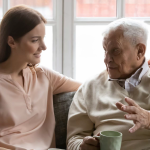 photo of an older man talking with a younder woman over a coffee infront of a bright window