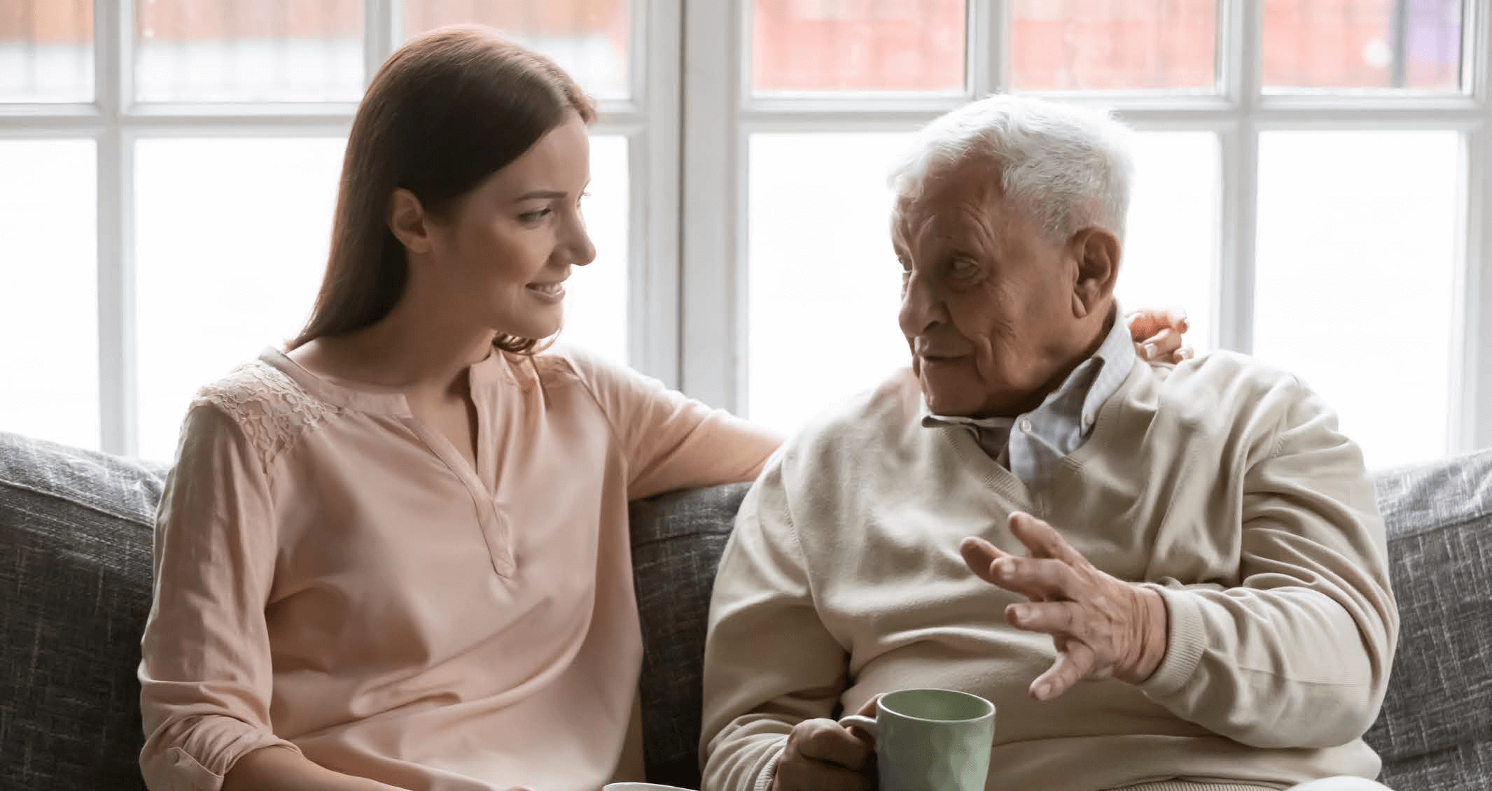 photo of an older man talking with a younder woman over a coffee infront of a bright window